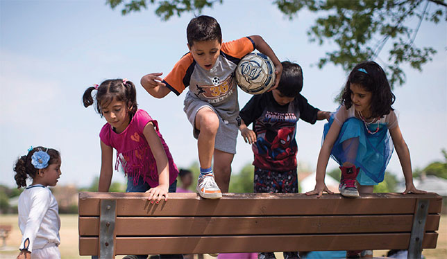 Des enfants réfugiés syriens s’amusent sur un banc de parc. Ils participaient, en juillet dernier à Toronto, à un camp de jour destiné à les aider à s’intégrer à l’école en septembre. Photo de The Canadian Press/Chris Young.